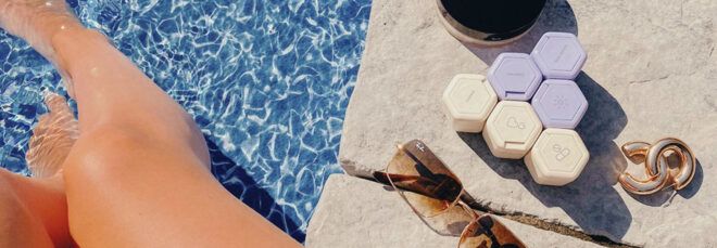 cream and purple travel containers, earrings, sunglasses by a pool