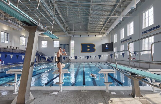 An indoor eight-lane swimming pool with a person getting ready to dive in to the water.