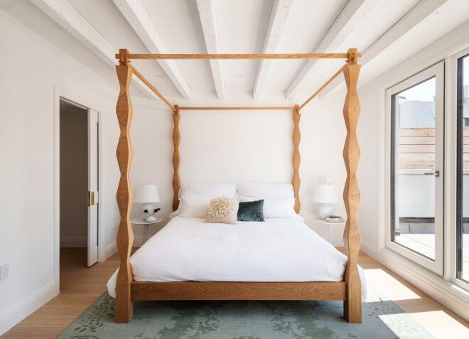 four-poster wood frame bed in white room