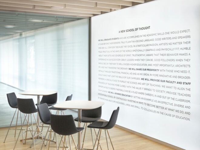 white tables and black chairs near white wall with text