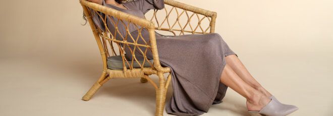 A person sitting in a wicker chair, wearing a taupe/gray dress.