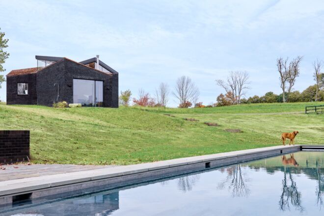 A lake with rolling green hills and a home with a black facade in the background.