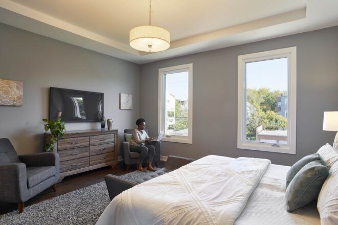 person sitting in chair in corner of room facing a large bed