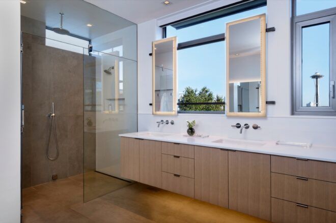 Dual sinks with tall rectangular mirrors in a bathroom with a glass-enclosed shower.