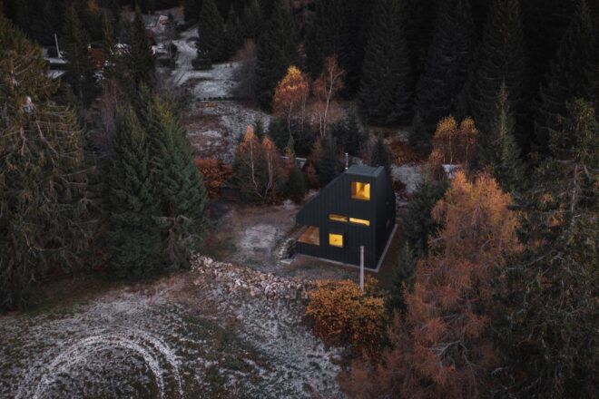 aerial view of angled black cabin in forest during autumn