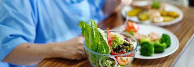 A person with their hand on a tray with bowls and plates of vegetables.
