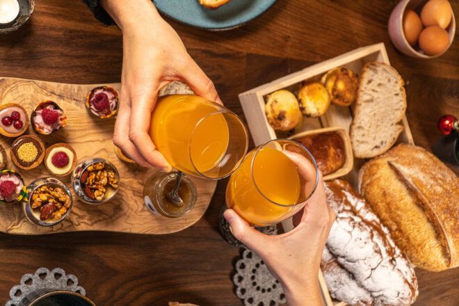 people clinking glasses of orange juice over a breakfast spread