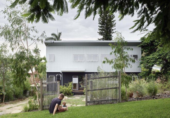 A person sitting in the grass just outside a gate surrounding the home.