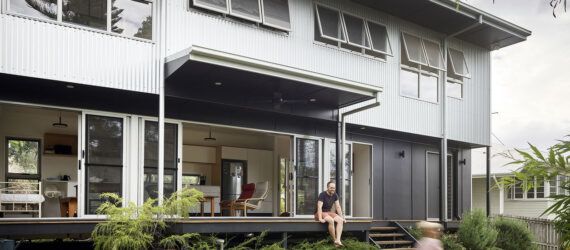 The exterior of a two-story home with a light and dark gray color scheme. A small deck is covered by an overhang, and it overlooks a green yard where a child runs around.