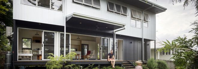 The exterior of a two-story home with a light and dark gray color scheme. A small deck is covered by an overhang, and it overlooks a green yard where a child runs around.