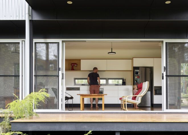 Open sliding glass doors look into a sitting room where two family members lounge.