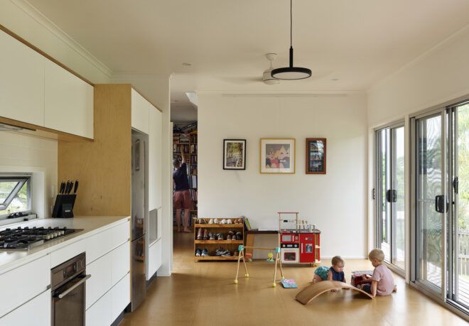 Two children playing in a living room with white walls and wood floors.