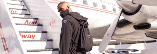 person boarding plane while wearing black jumpsuit and matching black face mask