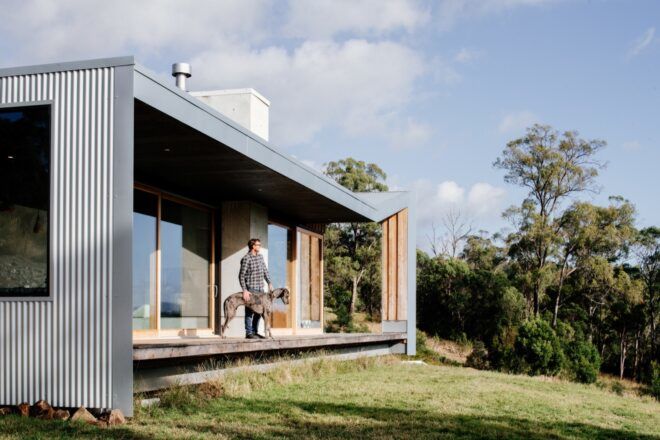 person and dog standing on narrow patio on small wood, metal and concrete home