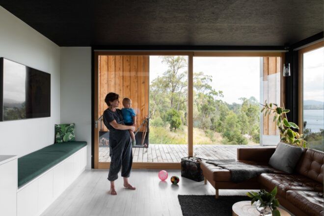 person holding baby and standing in front of brown leather sofa