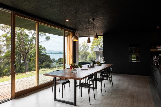 long, dark wood dining table near glass wall revealing river views