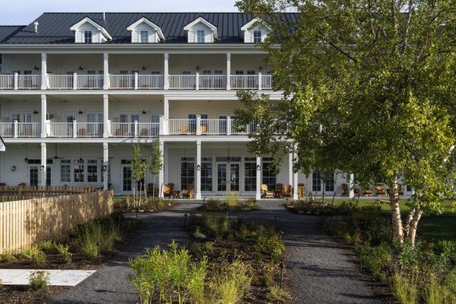 A three-story hotel facade with balconies and a green path leading up to the hotel.