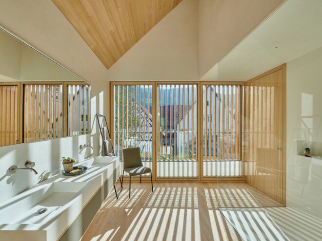 An interior room with light-toned wood ceiling, floor and walls. Sliding glass doors are covered with vertical blinds that let light into the room.