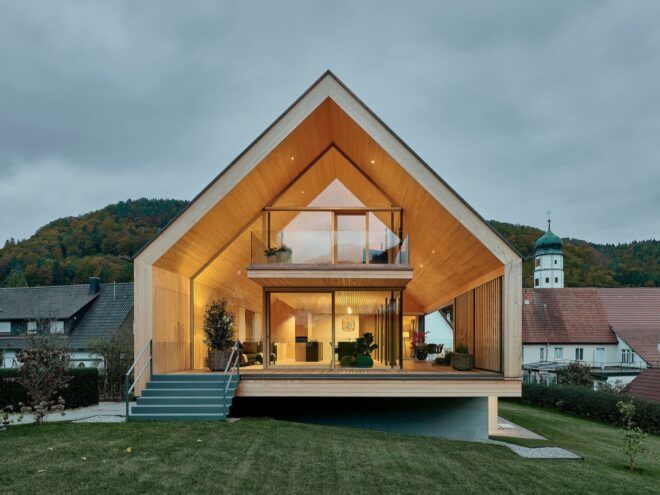 A traditionally-shaped home with a green lawn in front and glazed facade lit up from within.