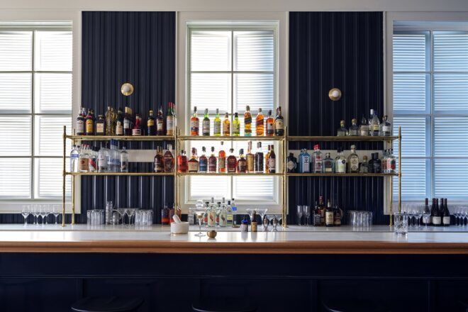 A fully stocked bar with deep blue curtains framing a window behind it.