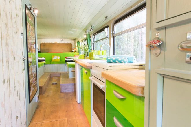 A kitchenette inside the bus with green accents and wood floors.