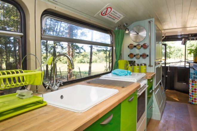 A kitchenette inside the bus with green accents, a sink and wood floors.