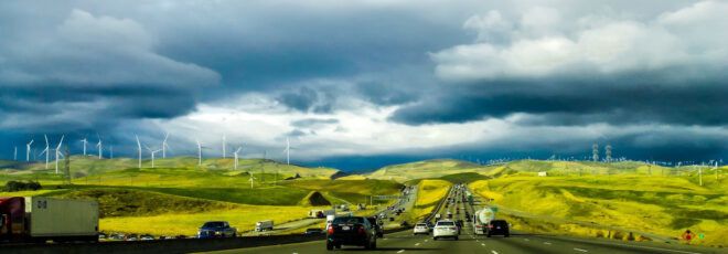 A road full of cars, surrounded by rolling green hills.
