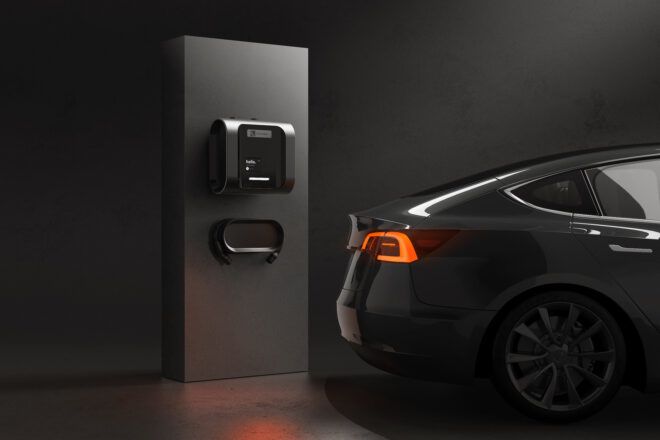 An EV charging box attached to a wall next to a black car.