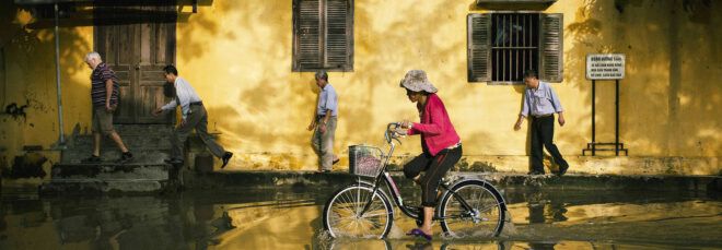 A flooded street with people walking and biking through the water.