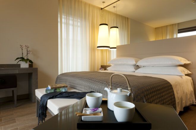 A hotel room with a bed in gray and white linens.