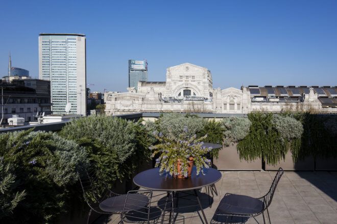 A green rooftop with a round table and two chairs that overlook Milan.