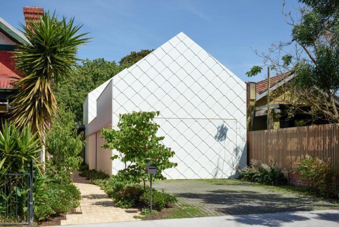 A house with a white cross-hatched facade and a traditional shape. Greenery surrounds the home.