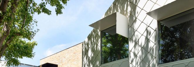 To the left, a tree. To the right, two windows on the facade of a house with a white, cross-hatched facade.