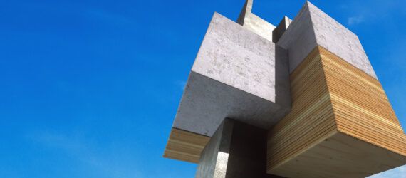 A cube-like structure of wood and concrete against a blue sky background.