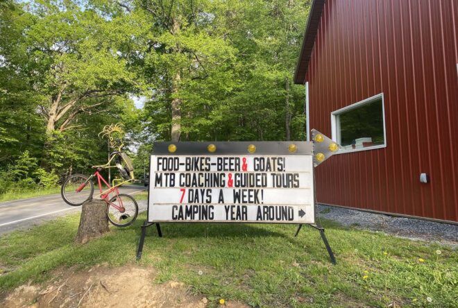 A sign in front of Arrowhead Bike Farm reading "Food-Bikes-Beer & Goats! MTB Coaching & guided tours 7 days a week! Camping year round."
