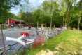A fence of bikes on the lawn in front of a red barn.