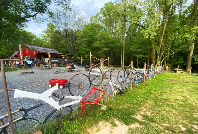 A fence of bikes on the lawn in front of a red barn.