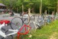 A fence of bikes on the lawn in front of a red barn.