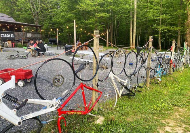 A fence of bikes on the lawn in front of a red barn.