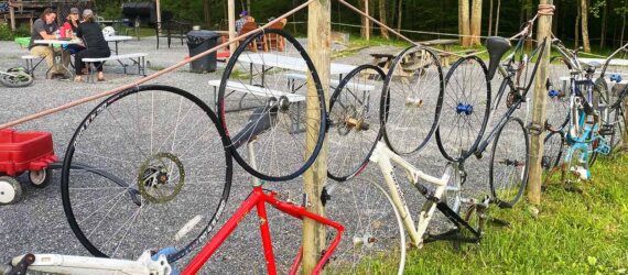 A fence of bikes on the lawn in front of a red barn.