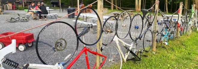 A fence of bikes on the lawn in front of a red barn.