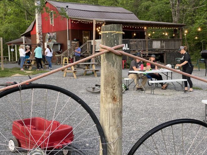 A fence of bikes on the lawn in front of a red barn.