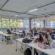 college students sitting at desks in room with large windows