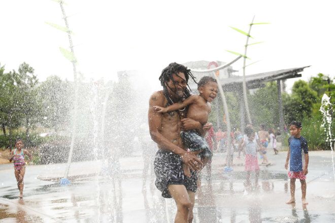 father and son playing in fountain at park