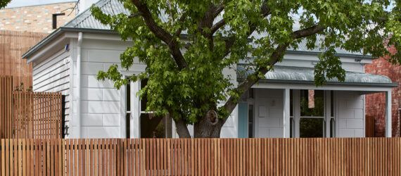tree and wood fence around old white house with brick extension in the back