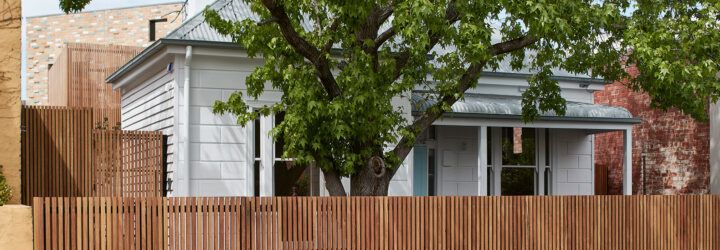 tree and wood fence around old white house with brick extension in the back