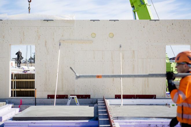 A wood wall being constructed, with a person passing from right to left.