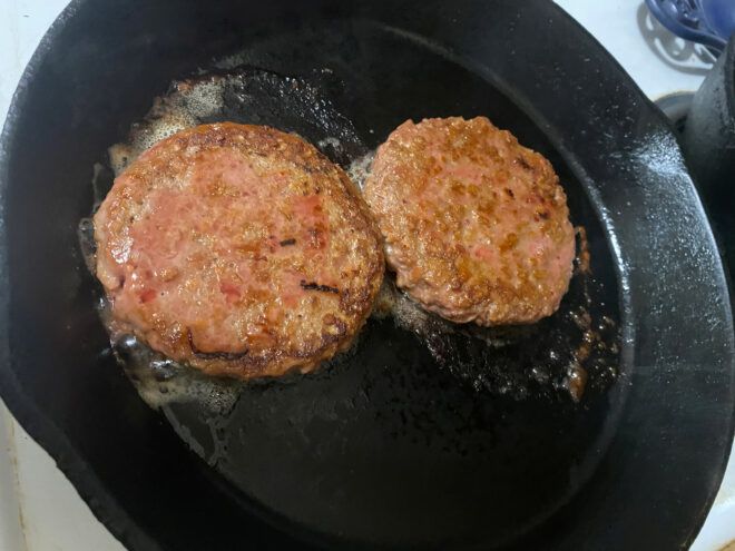 two sizzling Beyond burgers on cast iron skillet