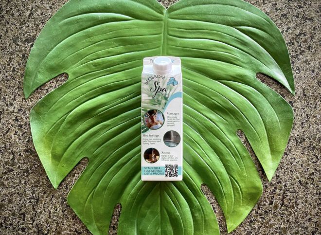 A carton of water resting on a green leaf background.