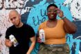 Two people standing against a wall holding cartons of FreeWater.